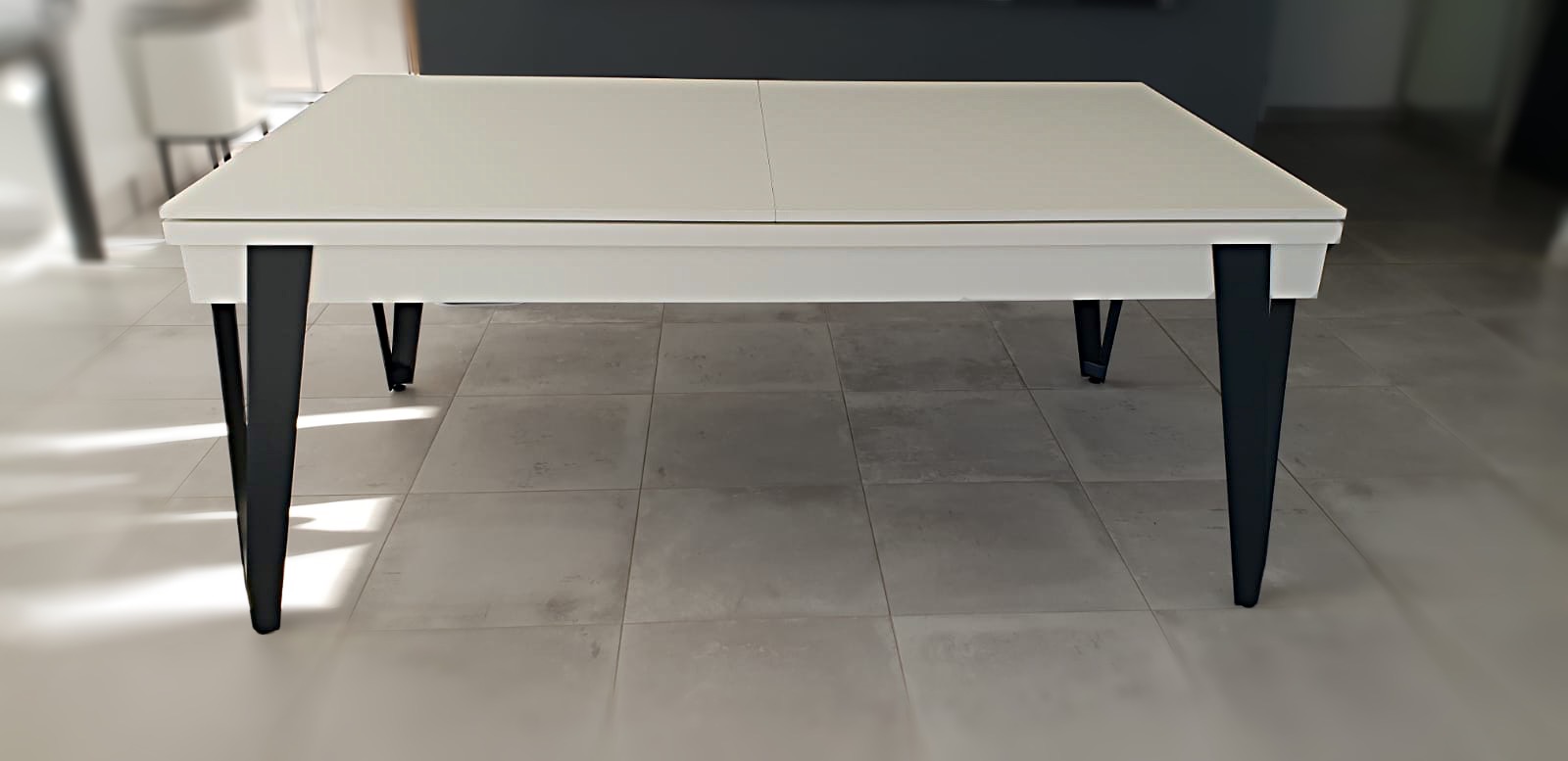 table moderne blanc mat au design léger, élégant porté par quatre pieds métalliques noir en forme de V qui se transforme en billard pure